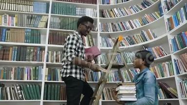 非洲男人一边站在梯子上一边从书架上挑选书籍，一边给大学里的非洲女孩送书